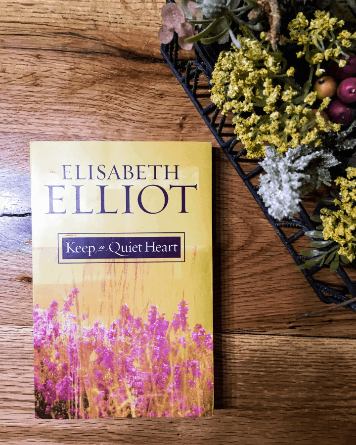 One of the best devotionals for moms by Elisabeth Elliot called Keep a Quiet heart on a piece of wood next to some flowers.