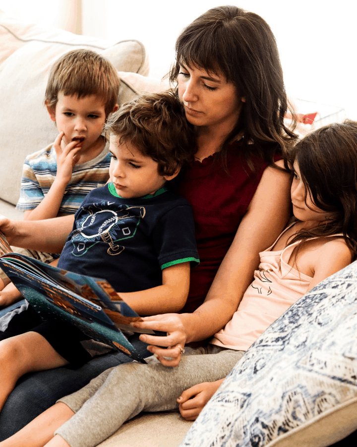 A mother reading a book to her three kids on a couch.